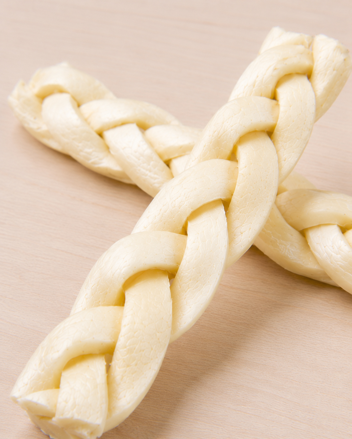 Allgood braided beef cheek chews, arranged in an X shape on a light beige wooden surface.