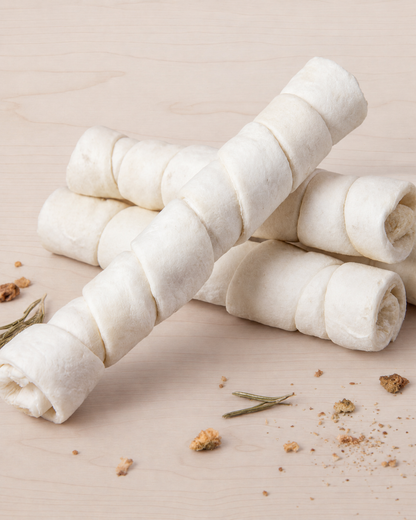 Rolled white beef chew on a beige background with rosemary and herbs.