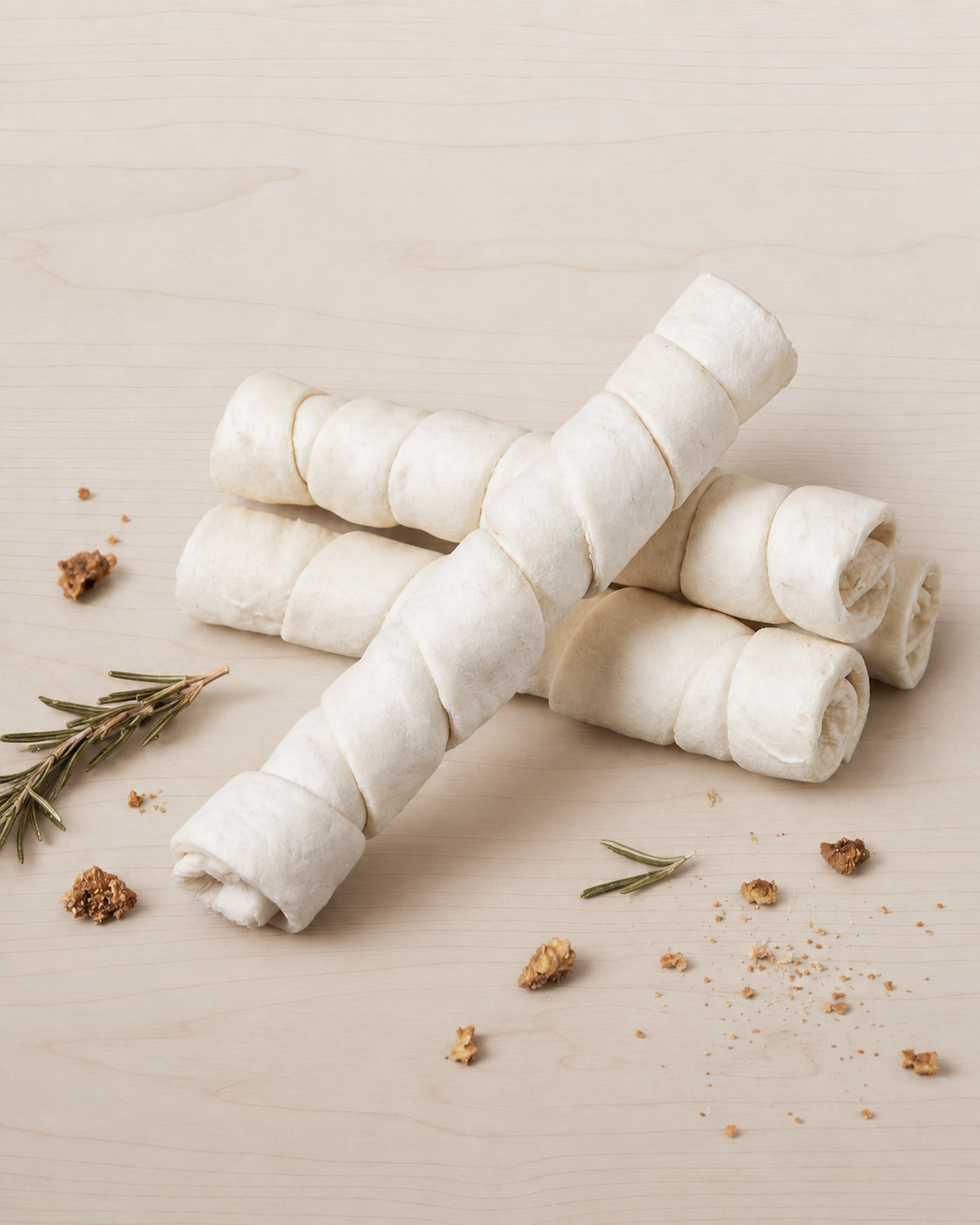Rolled white beef cheek on a beige surface with rosemary and small brown objects