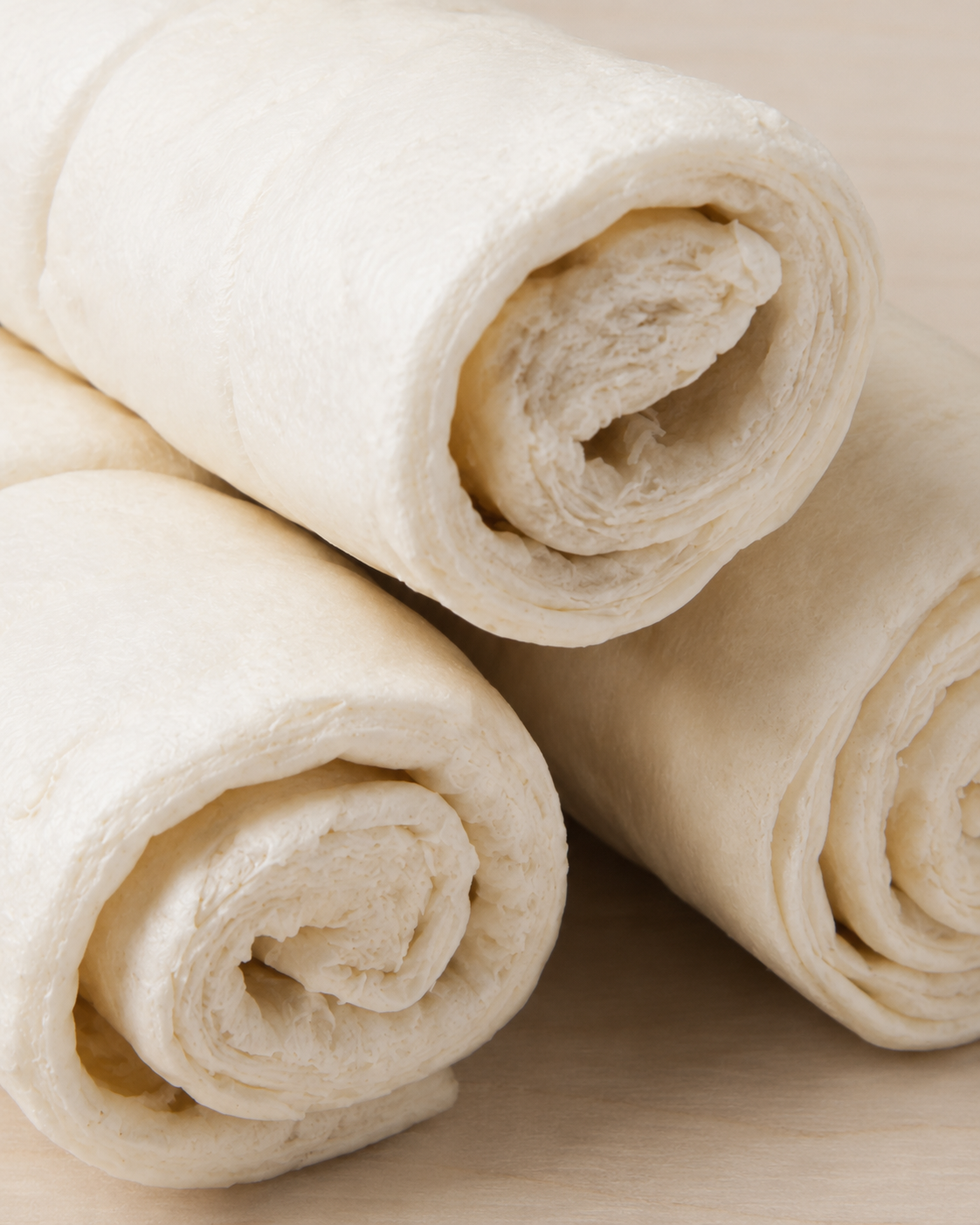Three beef cheek rolls arranged on a light wood surface.