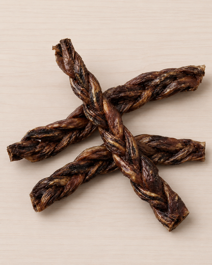 Four dark brown braided dog treats arranged in a cross shape on a light beige wood-grain background.
