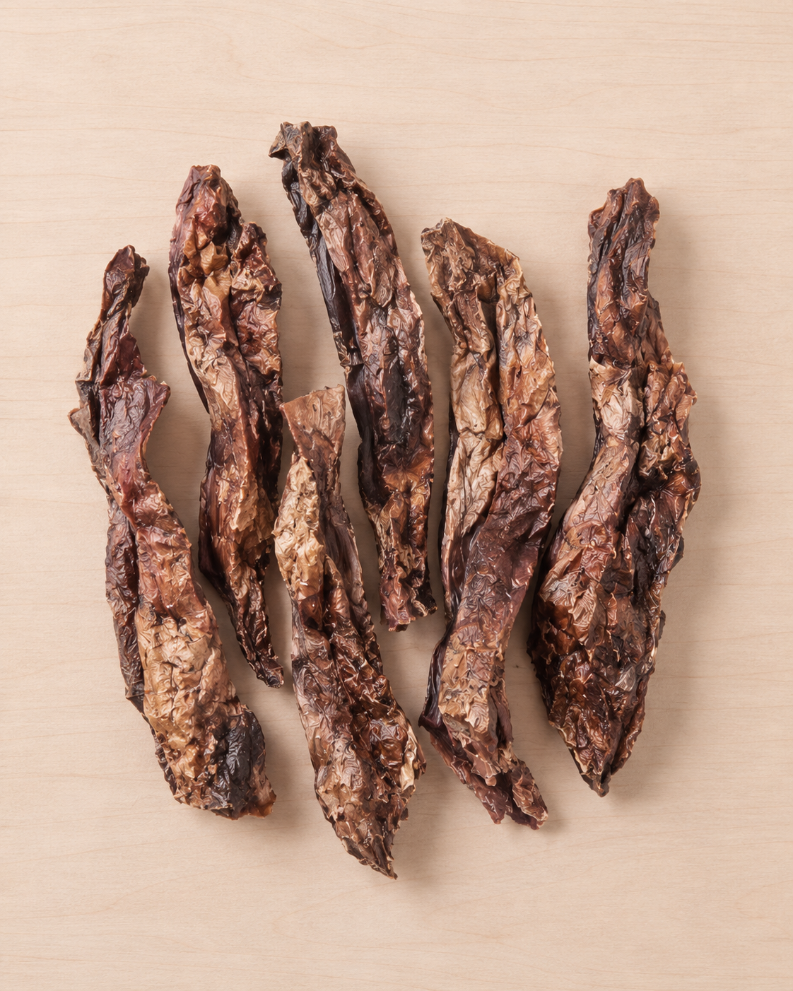 Five strips of dark brown jerky  arranged vertically on a light beige wood-grain surface.