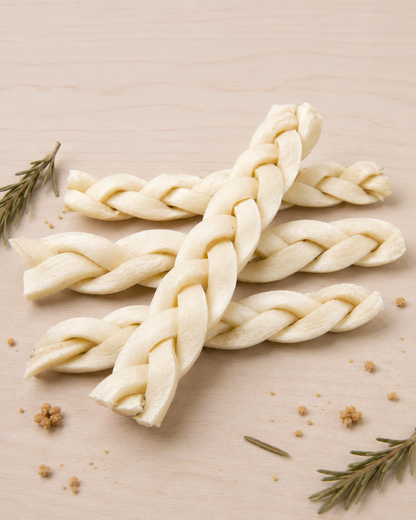 Four Allgood braided beef cheek chews, arranged on a light wood surface with small rosemary sprigs and crumbs.