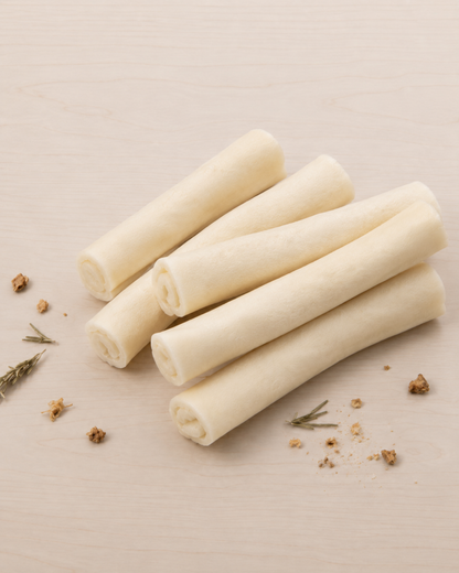 Beef chew bones arranged on a light wood surface with a few scattered herb crumbs and rosemary sprigs.