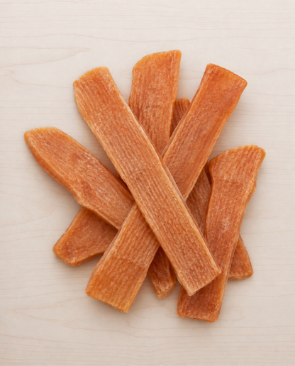 Several orange-brown dried carrot sticks or sweet potato chips arranged in a loose pile on a light beige surface.