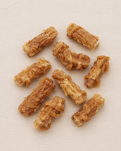 Nine dried, textured golden-brown sticks, likely beef jerky or dried meat snacks, arranged on a light beige wooden surface.
