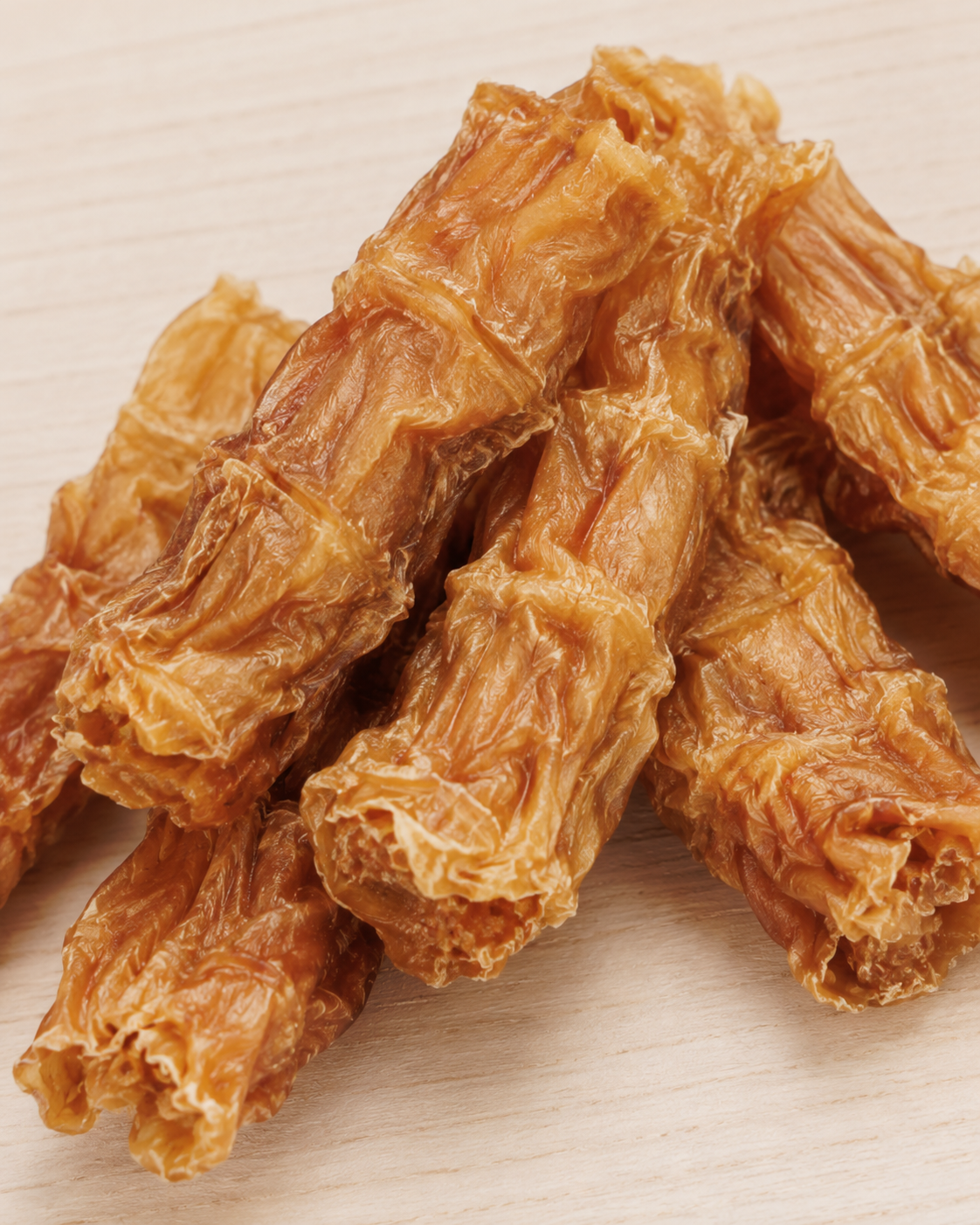 Several pieces of dried, wrinkled chicken dog treats piled on a light wood surface.
