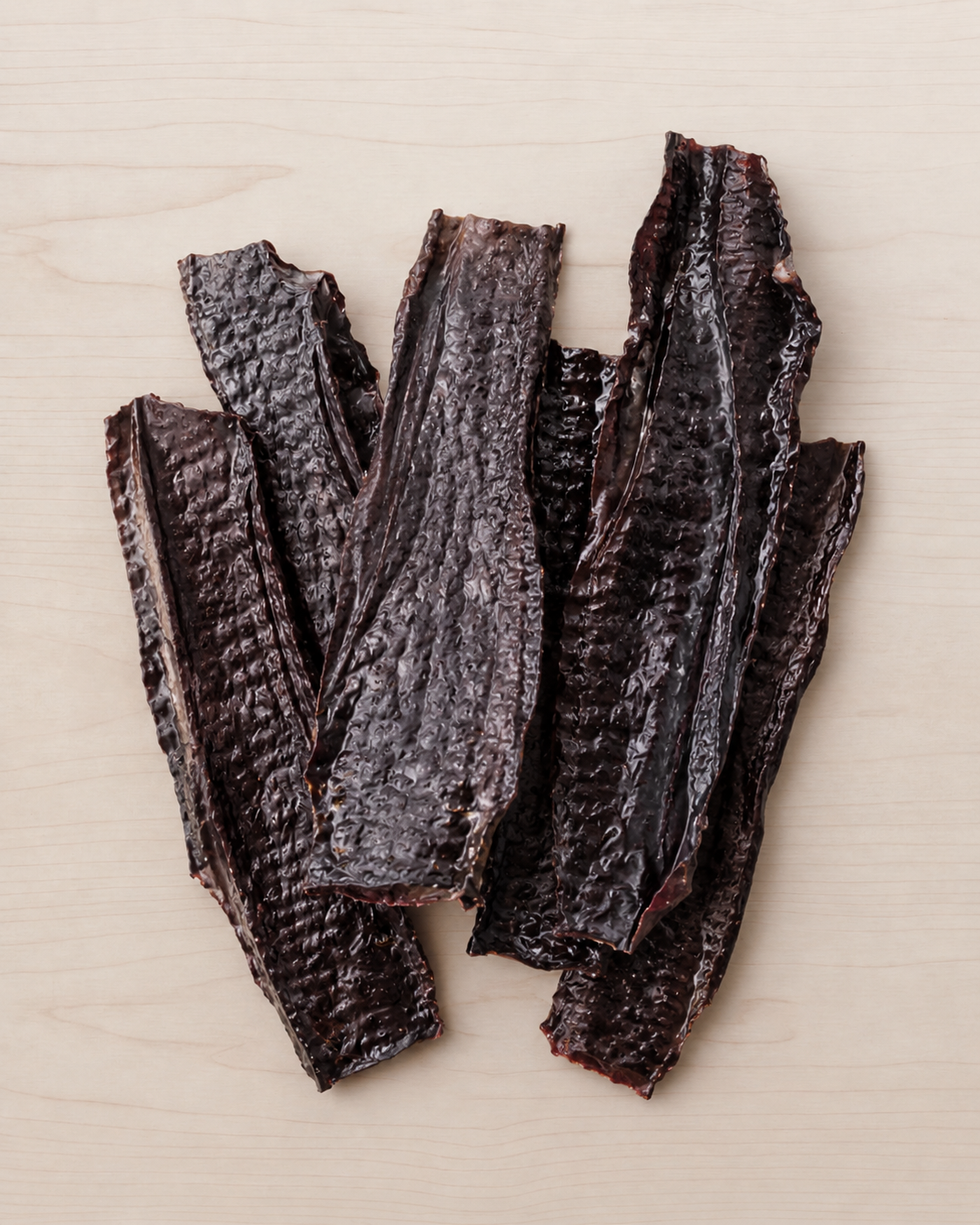 Several dark, wrinkled strips of dried jerky or smoked meat arranged on a light wood surface.