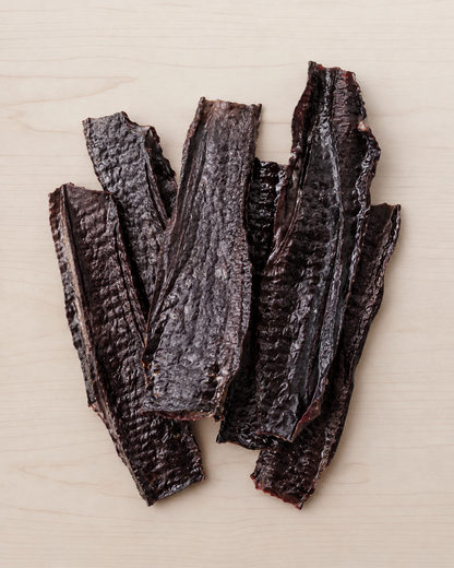 Several dark, wrinkled strips of dried jerky or smoked meat arranged on a light wood surface.
