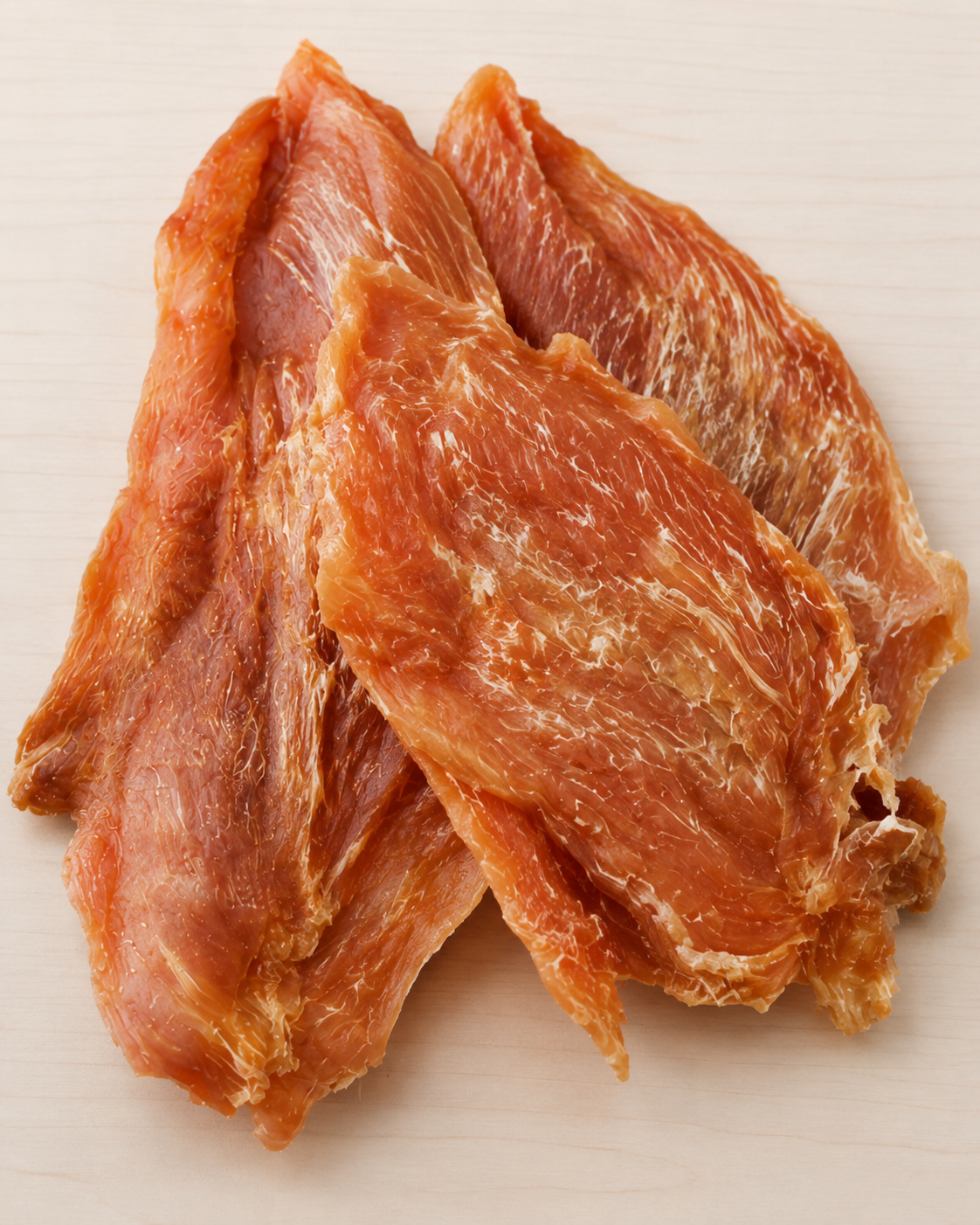 Three strips of dried, reddish-brown meat jerky stacked on a light beige surface.