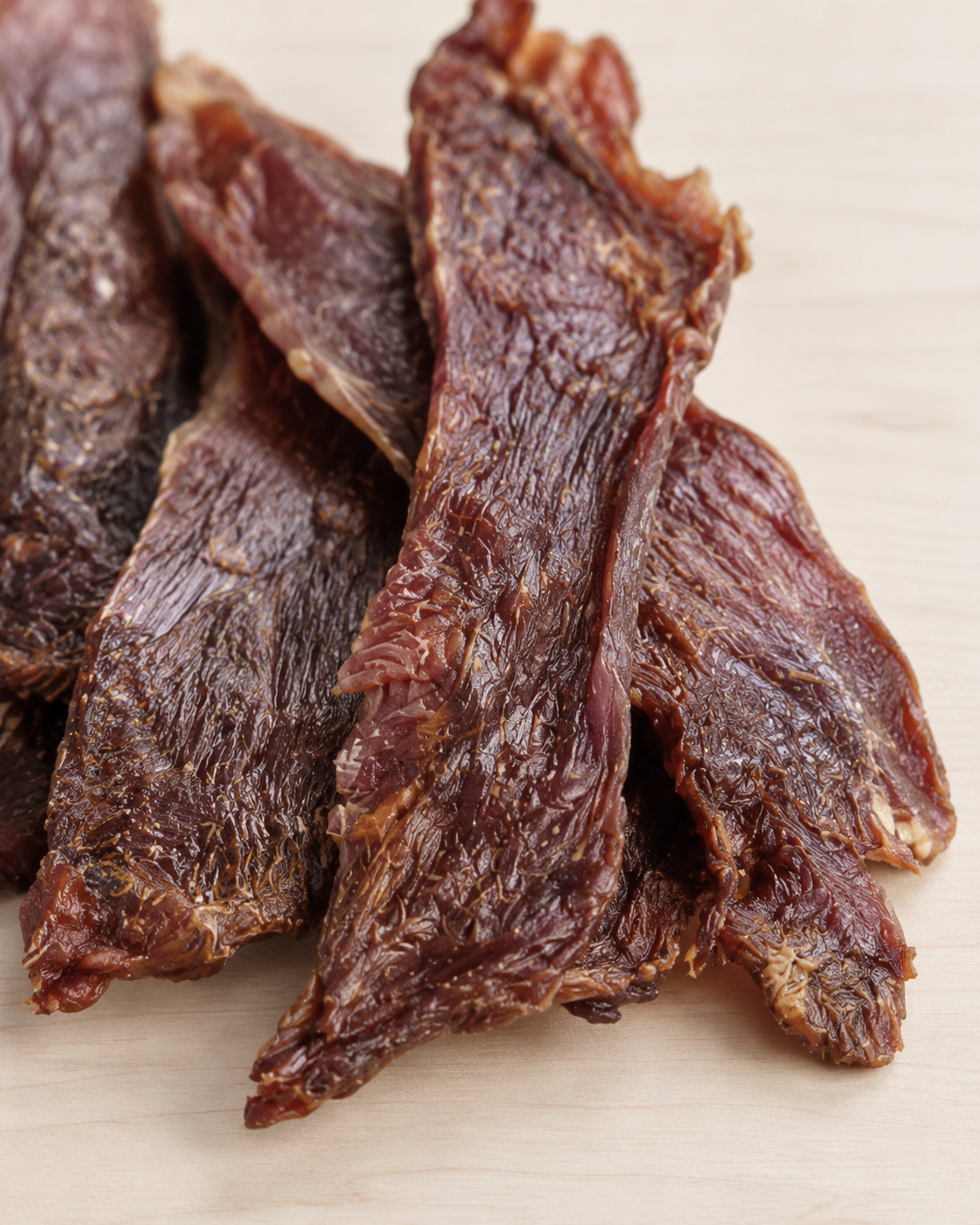 Several strips of duck jerky stacked on a light beige surface.