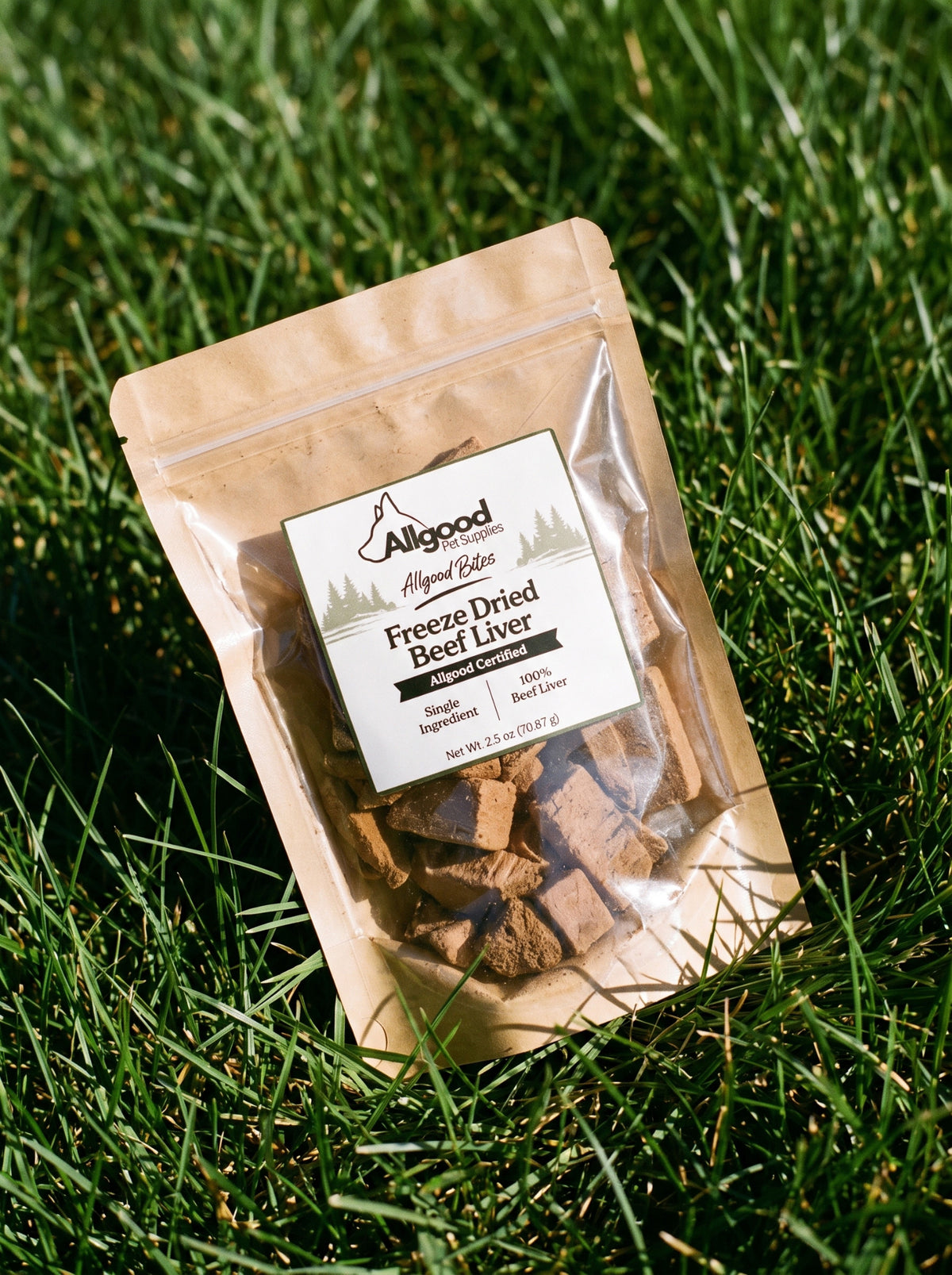 A stand-up pouch of Allgood Naturals Freeze Dried Beef Liver dog treats placed on green grass outdoors. The kraft paper pouch has a clear front window showing the freeze-dried treats inside, with a white product label on the front.