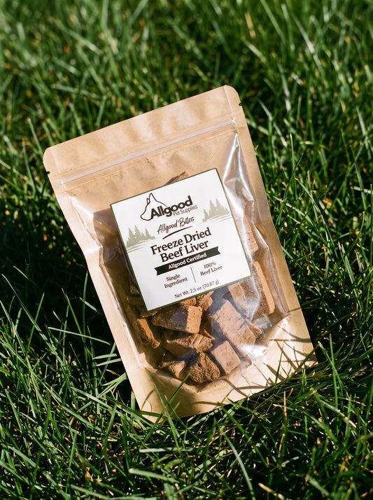 A stand-up pouch of Allgood Naturals Freeze Dried Beef Liver dog treats placed on green grass outdoors. The kraft paper pouch has a clear front window showing the freeze-dried treats inside, with a white product label on the front.
